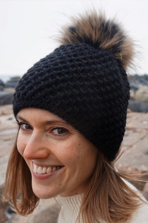 Schwarze Strickmütze IDA mit Bommel aus finnischem Waschbärfell.